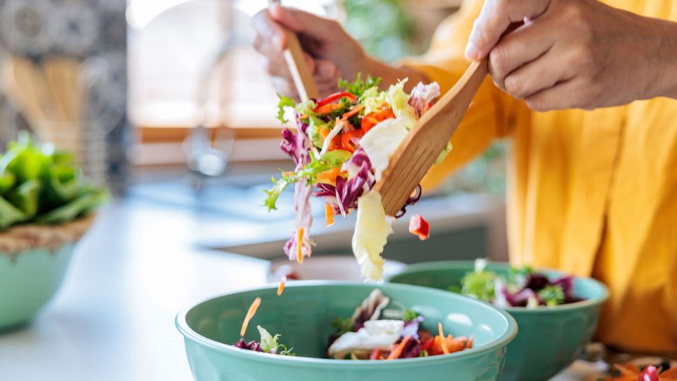 Close up of a persons hands, holding tongs, and tossing a healthy salad.