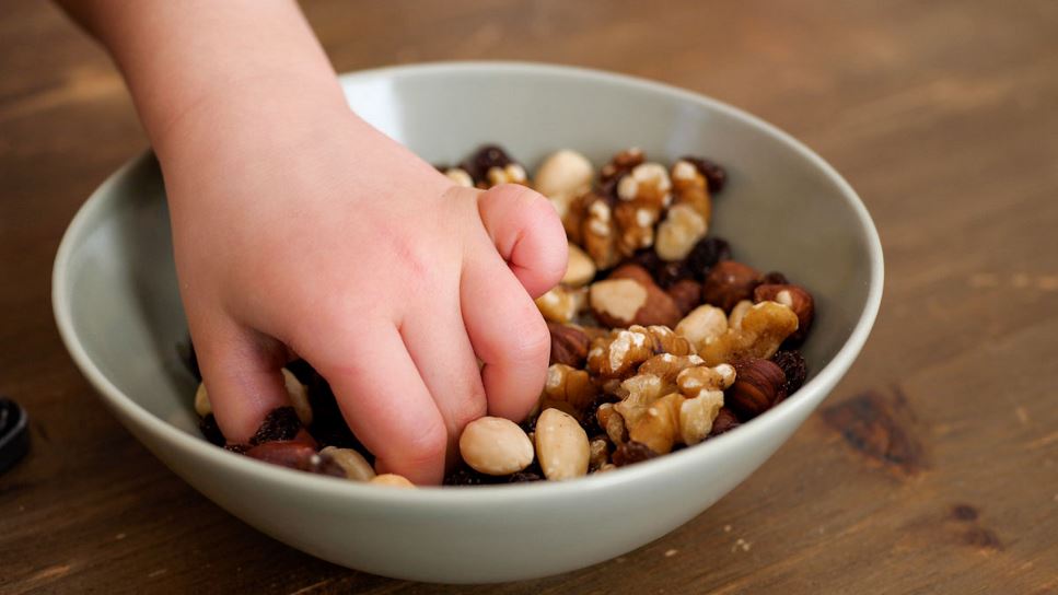 Close up of a child's hand grabbing a handful of mixed nuts.