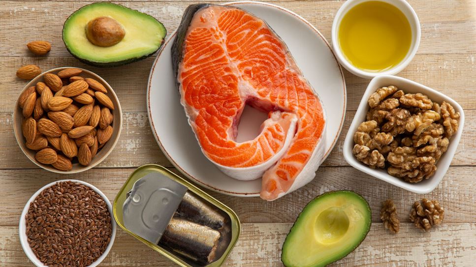 An assortment of foods with unsaturated fats, including salmon, canned fish, avocado, almonds, flax seed, walnuts and olive oil.