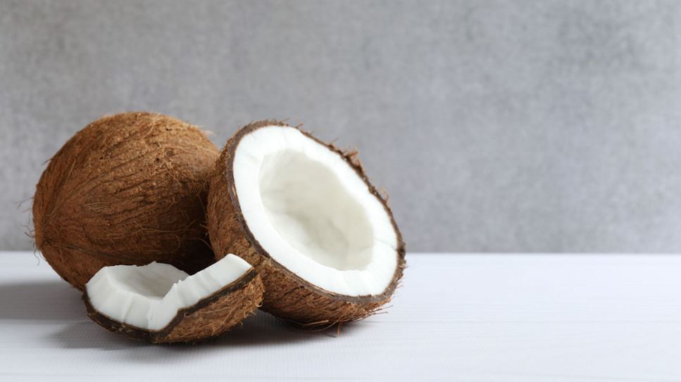 A coconut is split open, sitting next to a whole coconut.