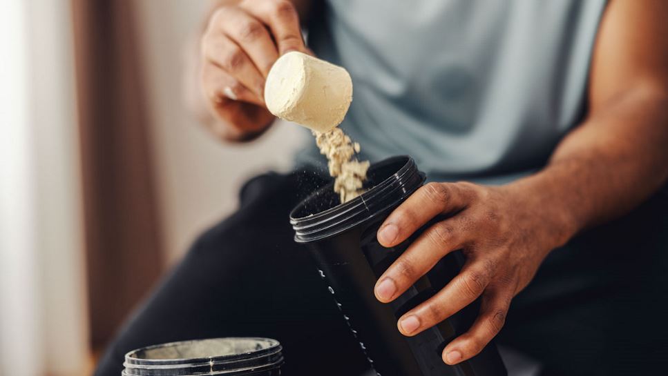 Close up of a man's hands scooping powder into a cup before a workout.