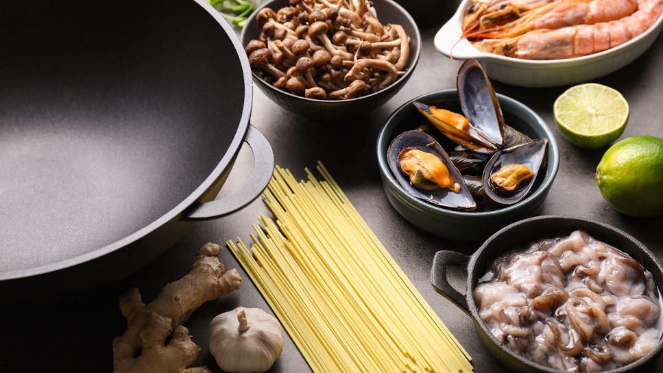 Prawns, mushrooms, noodles, mussels, lime, garlic and ginger sit next to an empty wok.