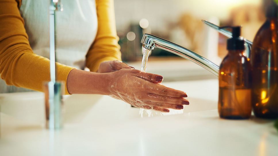 An individual washes their hands with running water, over a sink.