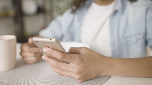Close up of teenager's hand scrolling on cellphone while eating breakfast