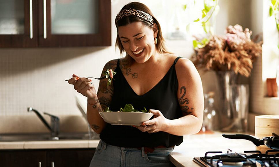 woman smiling and eating a salad in kitchen